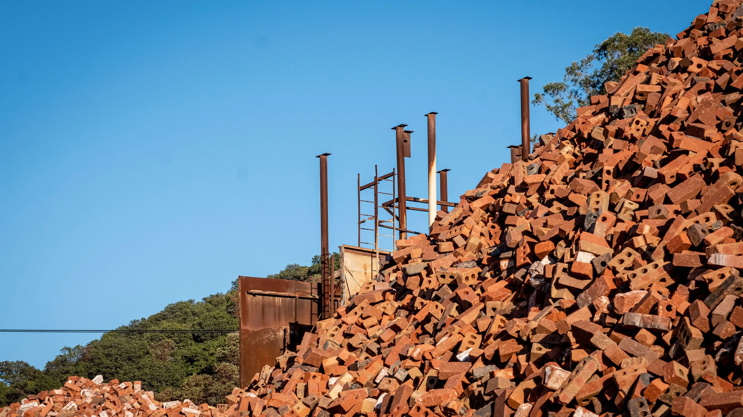 A reclamation yard's brick mountain against a clear sky, rusted steel columns still standing through it