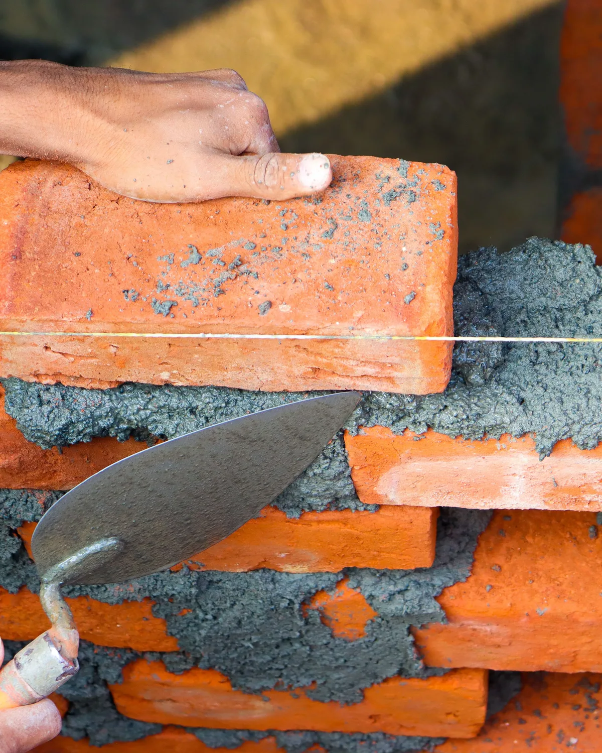 A bricklayer's hands bedding a brick to the string line, trowel in hand