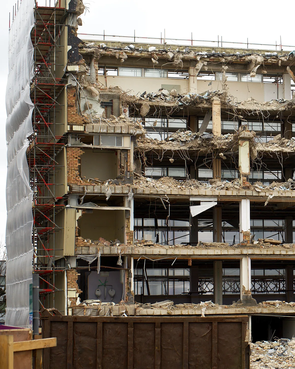 A multi-storey concrete building part-way through top-down demolition, floors stripped progressively behind scaffold