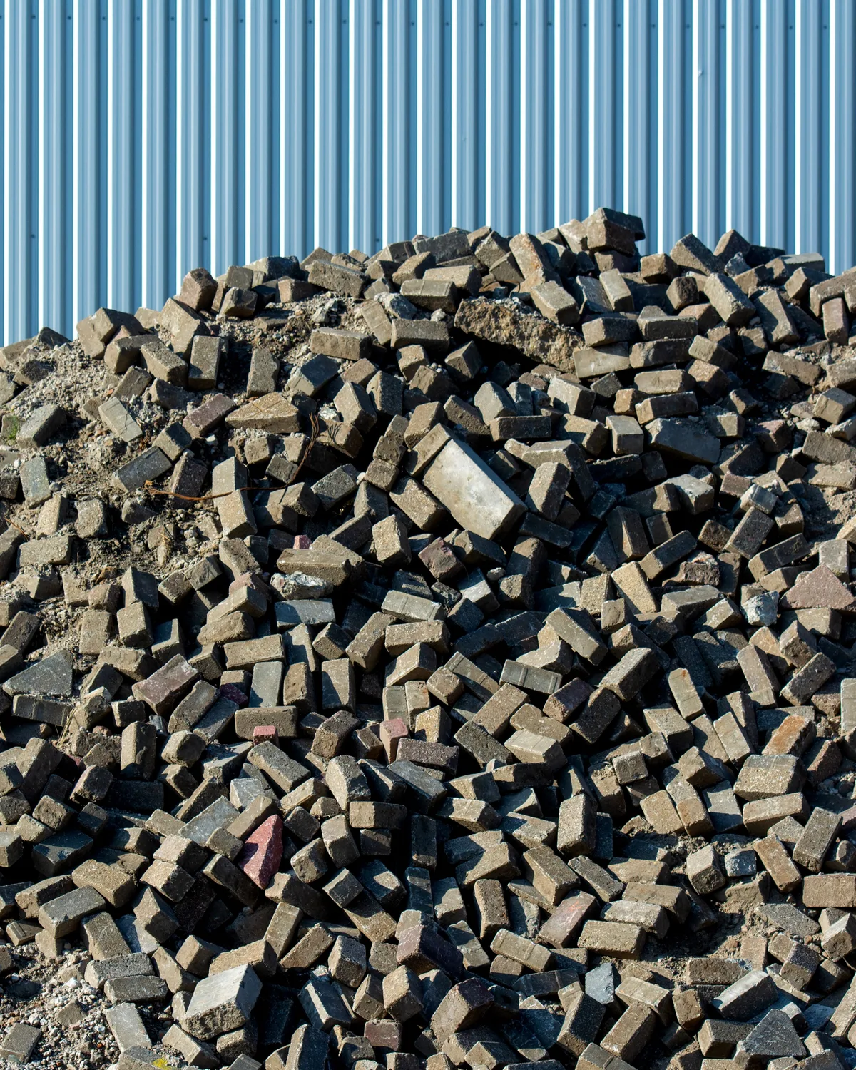 A sorted pile of reclaimed bricks against corrugated site cladding, waiting to be graded